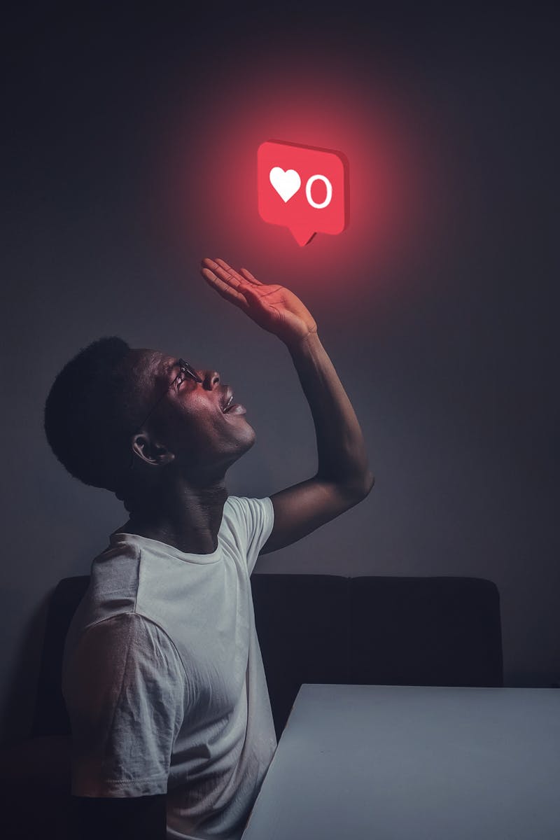 A man sits indoors reaching towards a glowing social media notification icon.